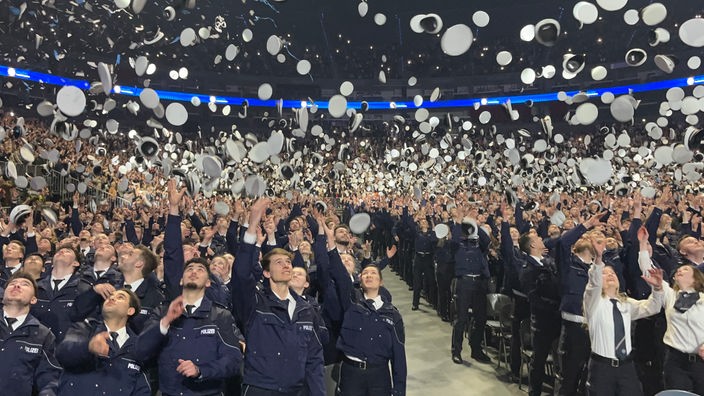 Tausende neue Polizisten werfen ihre Mützen in der Kölner Lanxess-Arena in die Luft.