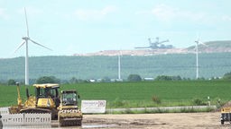 Baufahrzeuge stehen auf einem großen Feld, im Hintergrund sieht man einen Kohlebagger
