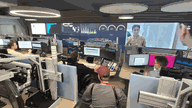 Man sieht großräumig den Arbeitsplatz des IT-Lagezentrums bestehend aus einigen Mitarbeitern, mit jeweils mehreren Computerbildschirmen