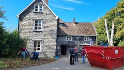 Verschiefertes altes Haus vor dem ein roter Bauschuttcontainer steht