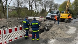 Auf dem Foto sieht man zwei Einsatzkräfte des Technischen Hilfswerk, die vor einer Baugrube stehen