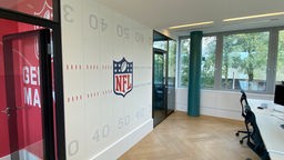 Hauptquartier von innen. Eine weiße Wand  auf dem das NFL-Logo in blau und rot zu sehen ist.