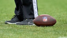 NFL Football liegt auf einer Wiese im Hintergrund sind Beine von jemanden zu erkennen.