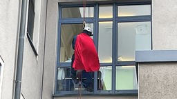 Mann im roten Umhang am der Fassade eines hohen Gebäudes