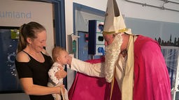 Ein Mann im Nikolaus-Kostüm in der Uniklinik begrüßt eine Frau mit einem Kleinkind auf dem Arm
