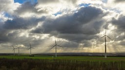 Die Sonne bricht durch die Wolkendecke oberhalb eines Felds in Grevenbroich, auf dem Windräder stehen