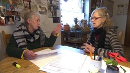 Zwei ältere Frauen sitzen am Küchentisch und sprechen miteinander 