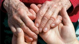 Junge Hände halten alte Hände - Symbol für die Bedürftigkeit älterer Menschen