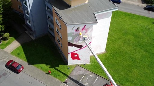 Drohnenaufnahme einer Hausfassade in Wuppertal, an dem die Künstlerin gerade mit einem Kran arbeitet