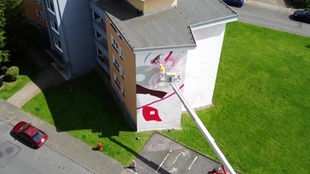 Drohnenaufnahme einer Hausfassade in Wuppertal, an dem die Künstlerin gerade mit einem Kran arbeitet