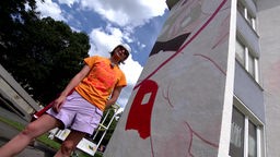 Künstlerin Juuri steht vor den ersten Teilen ihres Kunstwerks an einer Wuppertaler Hauswand