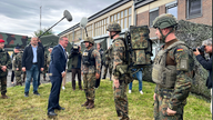 Zu sehen ist Boris Pistorius, wie er umgeben von einem Kamerateam drei Soldaten in Uniform vor der Kaserne begrüßt.