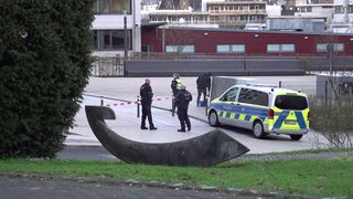 Auf dem Foto sind Polizisten, die um ein Absperrband an einem Wuppertaler Gymnasium herumlaufen. Daneben steht ein Polizeiauto.