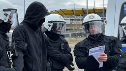 Polizisten mit einem maskierten Mann an einem Stadion