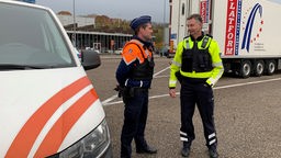 Ein deutscher und ein belgischer Polizist stehen zusammen auf einem Parkplatz