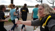 Eine Frau steht an einem Versorgungsstand. Sie reicht in ihrer rechten Hand einen Pappbecher mit Wasser an vorbeilaufende Läufer.