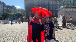 Ein Mann und eine Frau stehen mit Kostüm als Queen und mit England Farben verkleidet auf dem Rathausplatz