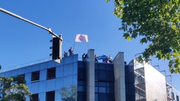 Die Arbeiter streiken auf einem Abrisshaus. Sie halten ein Plakat hoch: "Hungerstreik."