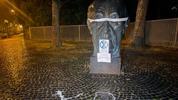 Eine Statue in Bonn ist mit einer Augenbinde maskiert. Auch ein Schild mit dem Logo von Estinction Rebellion hat sie umgehängt bekommen.