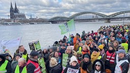 Menschen protestieren vor dem Rhein in Köln.