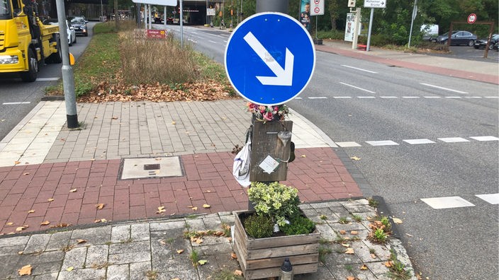 Die Unfallstelle in Rhiehl mit Blumengesteck an einem Verkehrsschild