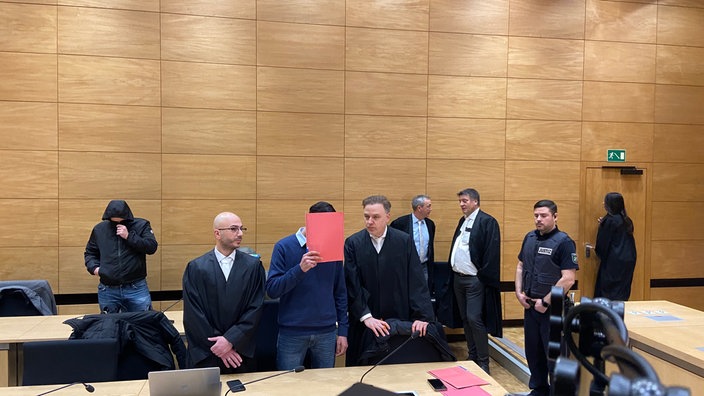 Hauptangeklagter Mwafak al S. hinter rotem Hefter Rechts daneben: Strafverteidiger Burkhard Benecken Im Hintergrund links: einer der mitangeklagten Deutschen