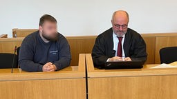 Der Angeklagte sitzt links neben seinem Anwalt auf der Anklagebank im Gericht