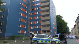 Das Bild zeigt ein Hochhaus, davor steht Polizei.