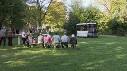 Auf einer Bierzeltbank sitzen Anwohner in Pulheim im Park vor einer kleinen Bühne 