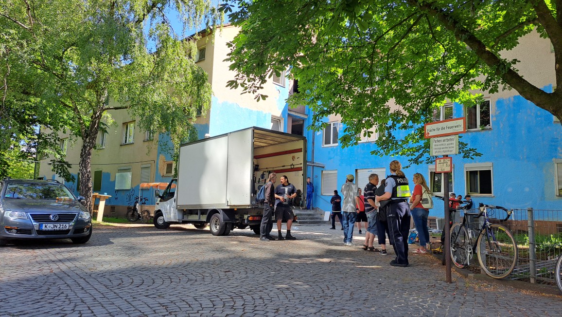 Ein Möbelwagen sowie mehrere Menschen vor einem blauen Haus