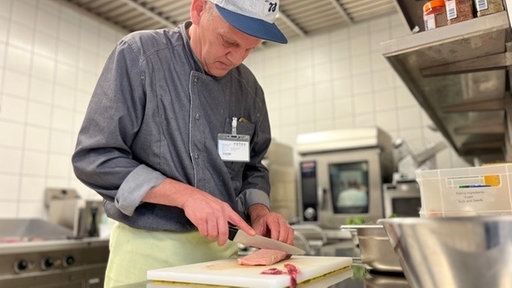 Mann mit Kappe und Messer in der Hand schneidet Fleisch