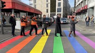 Bonner Oberbürgermeisterin Katja Dörner und weitere Verantwortliche stehen auf dem Zebrastreifen in Regenbogen-Farben-Optik.