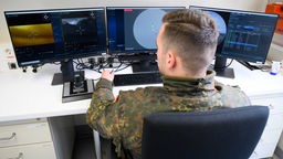 Ein Soldat vor drei Bildschirmen mit Radarbildern.