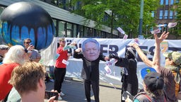 Viele Menschen werfen Papiergeldscheine, in der Mitte eine Person im Anzug und einer Gesichtsmaske