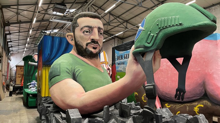 Ein Karnevalswagen mit der Darstellung: Selenskyj hält einen NATO-Soldatenhelm in der Hand und schaut ihn an