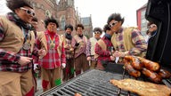 Kostümierte Menschen stehen in Aachen um einen Grill mit Würstchen herum