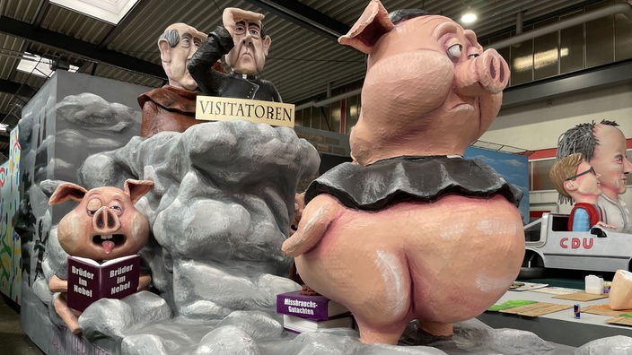 Der Mottowagen des Kölner Rosenmontagszugs zeigt zwei Schweine und zwei Männer und eine große Nebelwolke