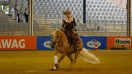 Die Ranging-Disziplin: Eine Frau reitet in einem Stadion mit Westernhut und Westernbluse auf einem hellbraunen Pferd.
