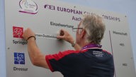 Ein Mitarbeiter der Reit-EM klebt den Namen Jeroen Dubbeldam, den Sieger im Springen, auf die Siegertafel.
