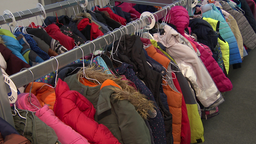 Auf dem Bild sind zwei Reihen Kleiderständer in einem Sozialkaufhaus zu sehen. Dort aufgehängt sind verschiedene Jacken.