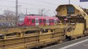 Im Hintergrund fährt eine rote S-Bahn im Bahnhof Troisdorf.