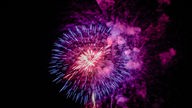Symbolfoto: Ein Feuerwerkskörper explodiert am Nachthimmel in pinken Farben.