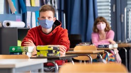 Zwei Schüler sitzen mit Masken im Klassenraum und lauschen dem Unterriht