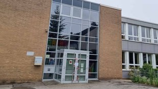 Eingangsbereich der Grundschule mit Galsfassade und einer Doppeltüre, die mit Flatterband versperrt ist