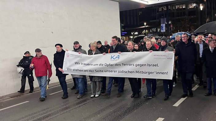 Das Bild zeigt eine Menschenmenge an deren Front sich ein Banner mit dem Schriftzug ''Wir trauern um die Opfer des Terrors gegen Israel.'' befindet.