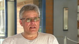 Ein Mann mit Brille und grauen Haaren spricht zur Kamera