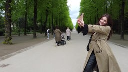 Auf dem Foto ist eine junge Frau mit roten Haaren, die ein Selfie im Düsseldorfer Hofgarten aufnimmt.