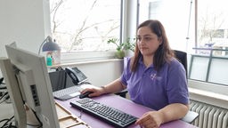 Frau in lilafarbenen T-Shirt mit Aufschrift des Pflegedienstes sitzt an einem Schreibtisch vor einer Tastatur