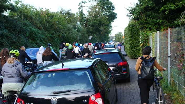 Schüler auf Fahrrädern und Autos drängeln sich auf einer schmalen Straße