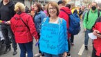 Eine Frau steht in einer Menschenmenge und trägt ein blaues Plakat um den Hals